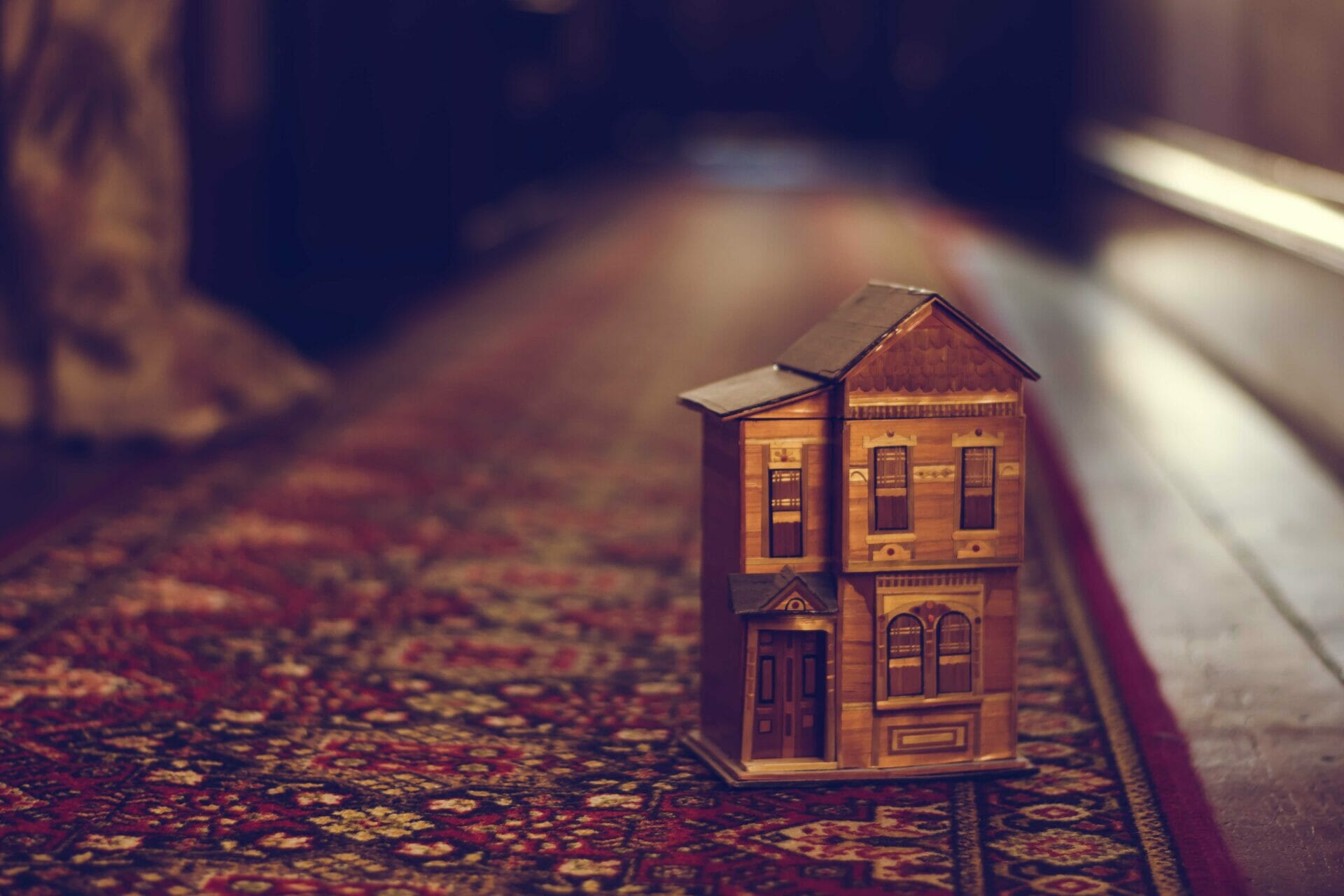 Een lief, klein houten speelgoedhuisje op een perzisch tapijt in de gang