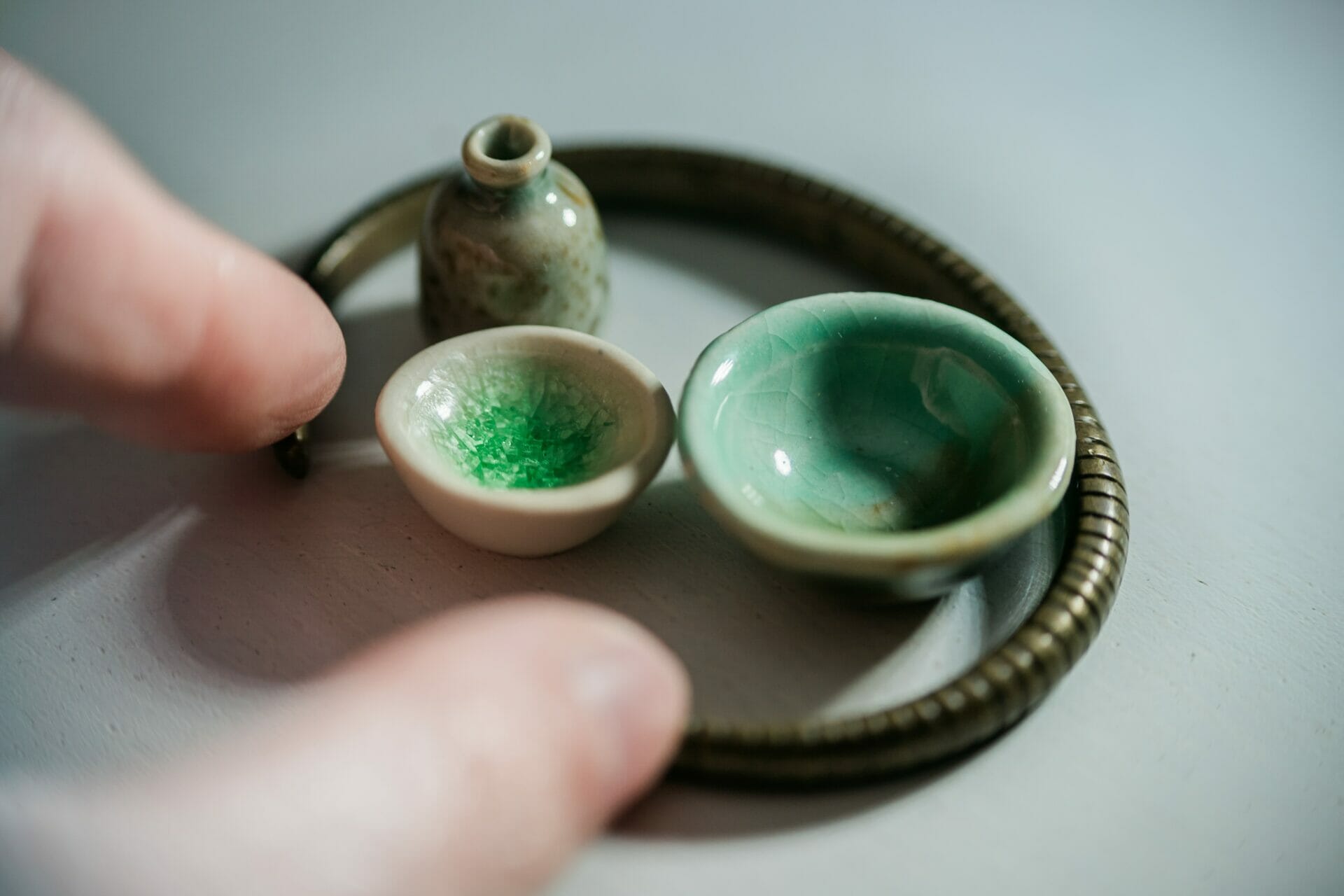 Miniatuur keramisch serviesgoed in cirkel bijeengehouden tussen duim en wijsvinger